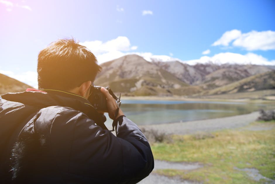 Back view of a photographer taking pictures of a serene mountain and lake scene on a sunny day.