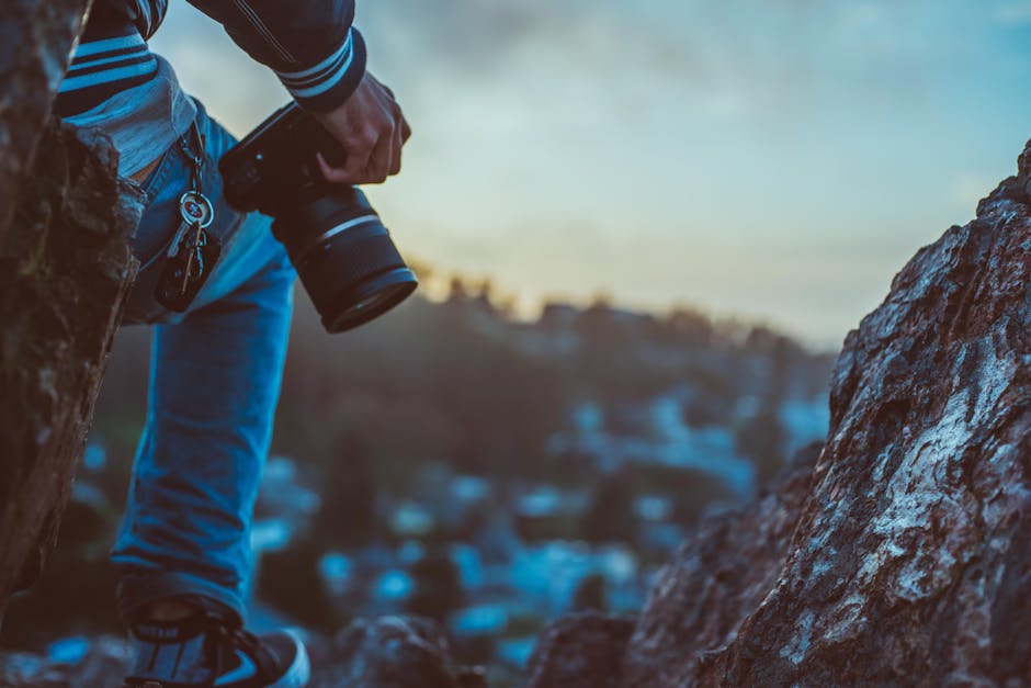 Photographer with camera outdoors on rocks during sunset capturing the scenic view.