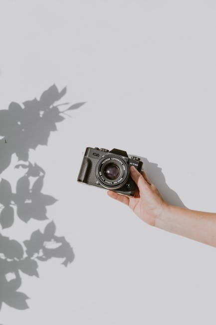 A hand holds a vintage camera against a white background, casting a shadow.